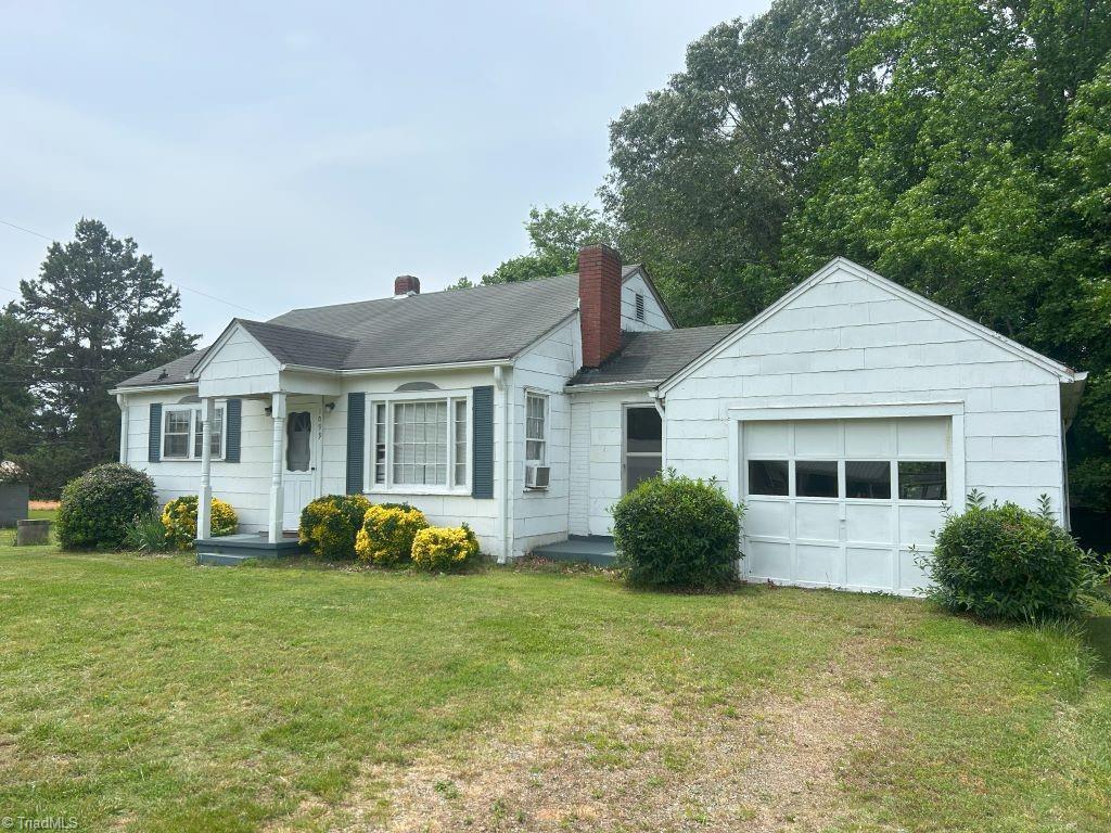 view of front of house with a chimney, a front lawn, a garage, cooling unit, and driveway