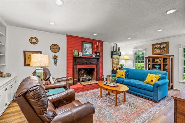 living room with light wood-style floors, a brick fireplace, a textured ceiling, ornamental molding, and recessed lighting