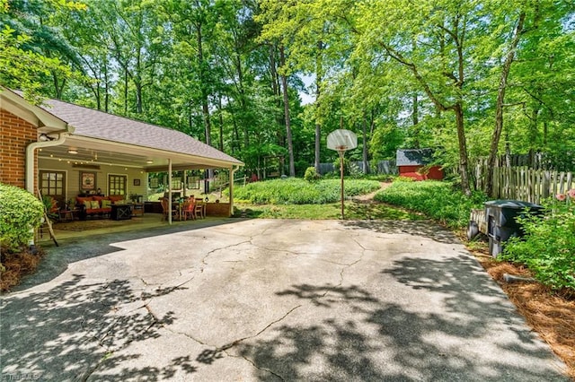 view of patio / terrace with driveway, fence, view of wooded area, and an outbuilding
