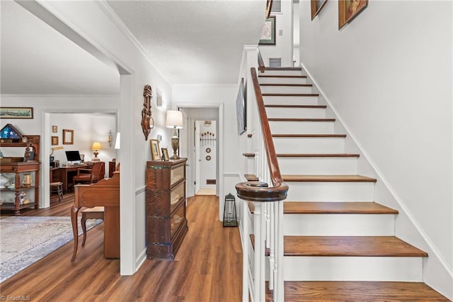 staircase with wood finished floors, ornamental molding, and a textured ceiling
