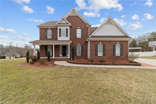 view of front of home with covered porch, a front lawn, fence, and brick siding