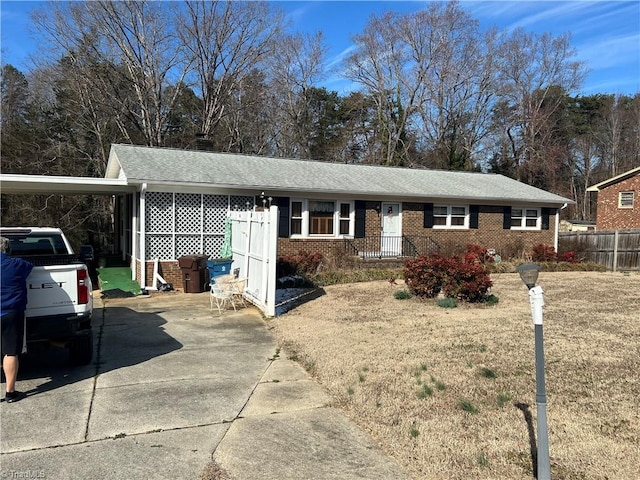 ranch-style home with brick siding, a shingled roof, fence, an attached carport, and driveway