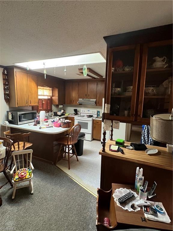 kitchen featuring white electric stove, light countertops, stainless steel microwave, a textured ceiling, and extractor fan