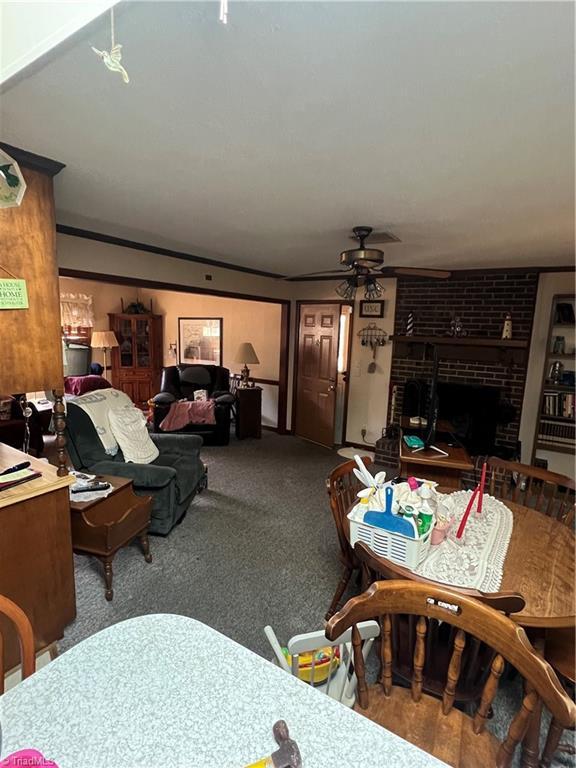 carpeted living room featuring a brick fireplace and ceiling fan