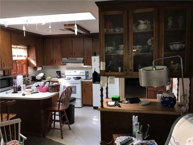 kitchen with white appliances, a breakfast bar area, a peninsula, ventilation hood, and light countertops