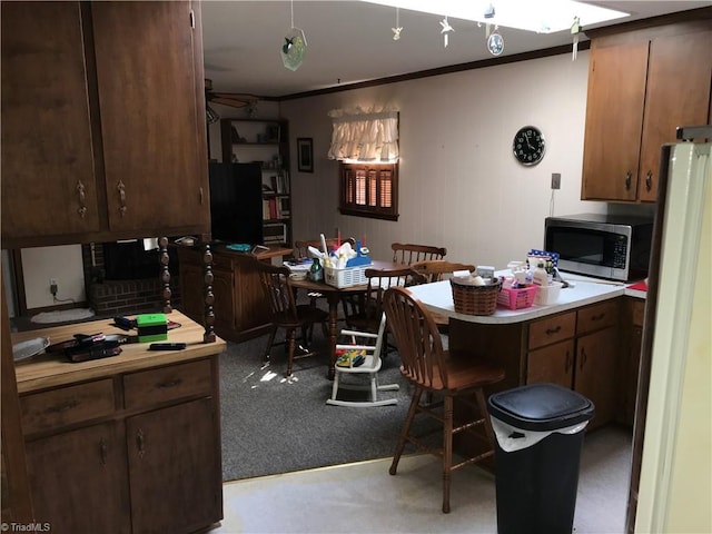 kitchen with light countertops, freestanding refrigerator, stainless steel microwave, and dark brown cabinetry