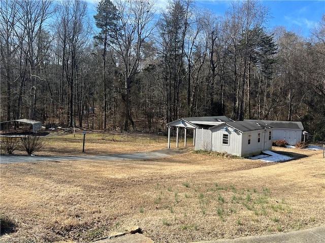 view of yard with a carport, a wooded view, and fence