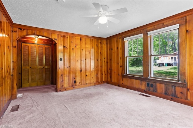 spare room featuring crown molding, wooden walls, ceiling fan, a textured ceiling, and light colored carpet