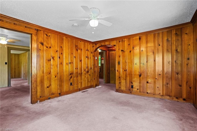 spare room featuring wooden walls, ceiling fan, ornamental molding, a textured ceiling, and light colored carpet