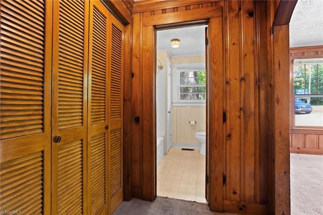 corridor featuring dark colored carpet, crown molding, a textured ceiling, and a wealth of natural light