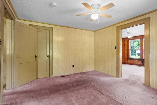 empty room with wood walls, ceiling fan, light colored carpet, and a textured ceiling