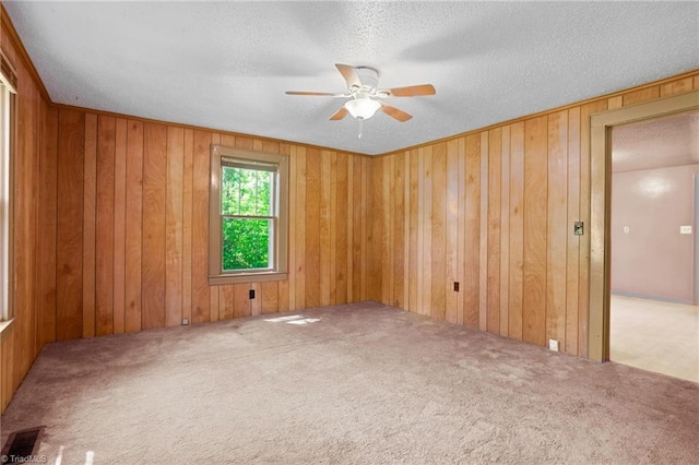 carpeted empty room featuring ceiling fan, wood walls, and a textured ceiling