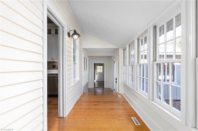 corridor with visible vents, light wood-style flooring, and vaulted ceiling