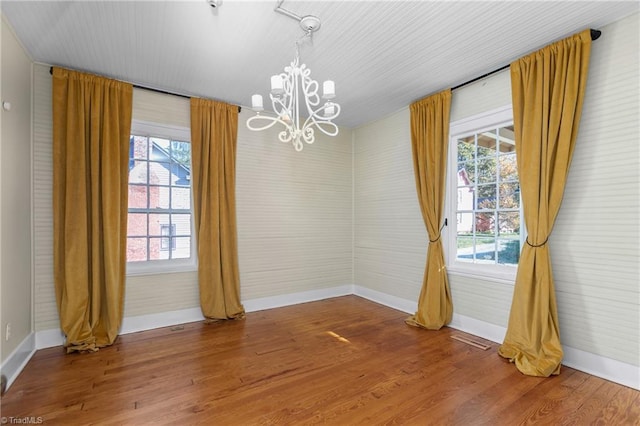 unfurnished room featuring a notable chandelier, wood finished floors, baseboards, and a wealth of natural light