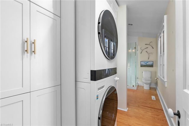 washroom featuring baseboards, laundry area, stacked washing maching and dryer, and light wood-style floors