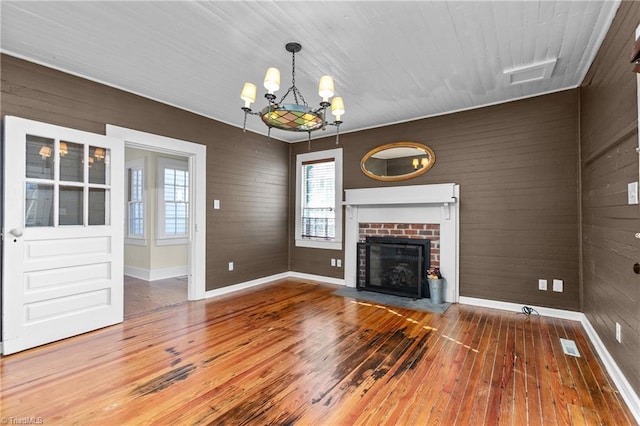 unfurnished living room featuring a chandelier, a brick fireplace, wood walls, and hardwood / wood-style flooring