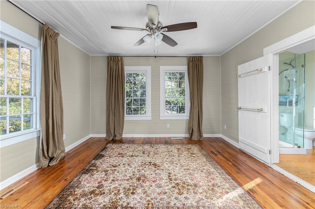 spare room featuring hardwood / wood-style floors, baseboards, visible vents, and a ceiling fan