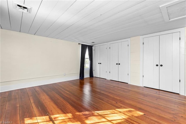 unfurnished bedroom featuring attic access, visible vents, wood-type flooring, and multiple closets