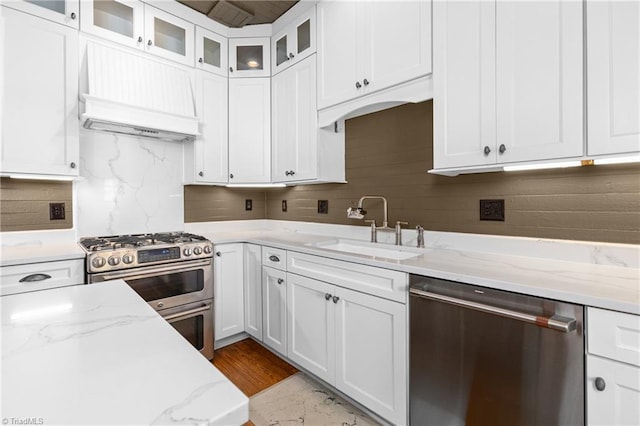 kitchen featuring premium range hood, a sink, stainless steel appliances, glass insert cabinets, and white cabinetry