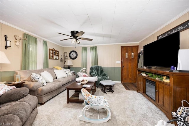 living area featuring wood walls, a glass covered fireplace, a ceiling fan, and crown molding