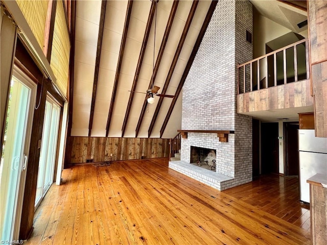 unfurnished living room featuring light hardwood / wood-style flooring, a brick fireplace, beam ceiling, high vaulted ceiling, and brick wall