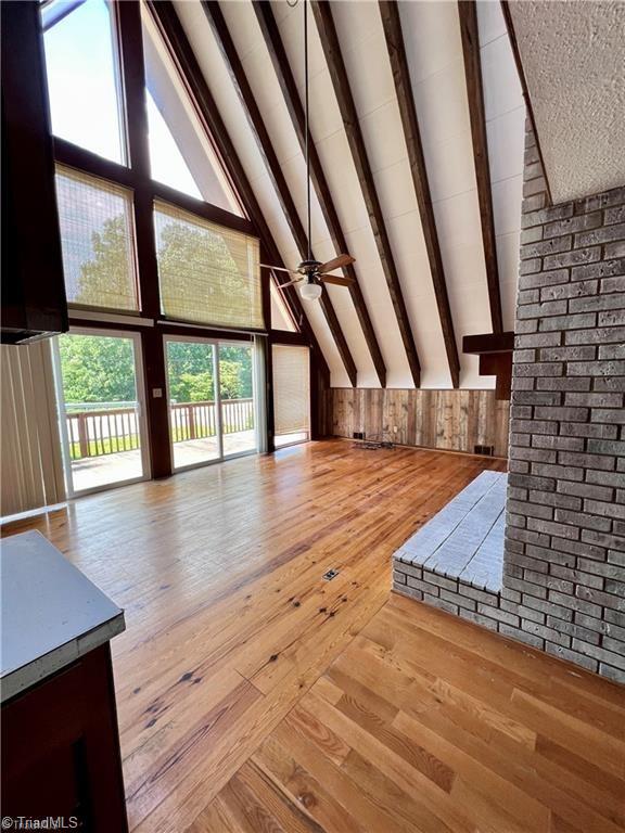 bonus room with light hardwood / wood-style flooring, ceiling fan, beamed ceiling, brick wall, and high vaulted ceiling