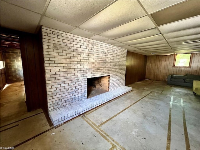 basement with a fireplace, wood walls, brick wall, and a drop ceiling