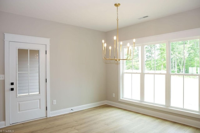unfurnished dining area with a chandelier, baseboards, and light wood finished floors