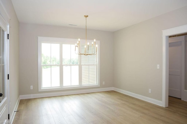 spare room featuring a chandelier, baseboards, and light wood-style floors