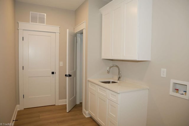 clothes washing area featuring washer hookup, light wood finished floors, baseboards, and cabinet space