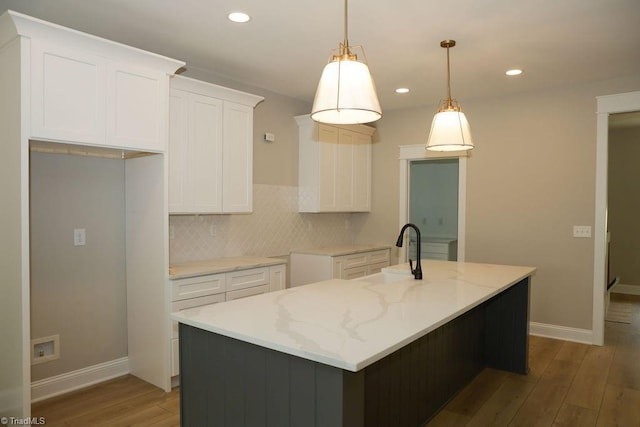 kitchen featuring a sink, baseboards, wood finished floors, a center island with sink, and white cabinetry