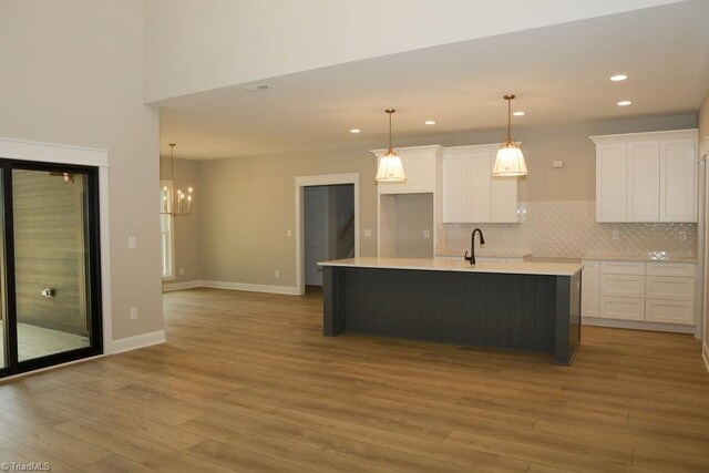 kitchen with white cabinets, light wood-style floors, an island with sink, tasteful backsplash, and recessed lighting