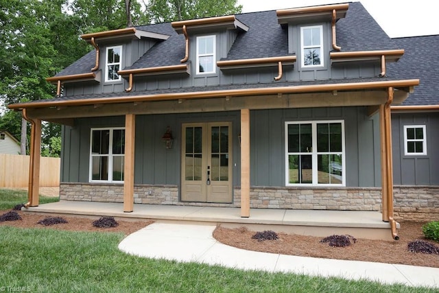 view of front facade with board and batten siding, covered porch, stone siding, roof with shingles, and fence