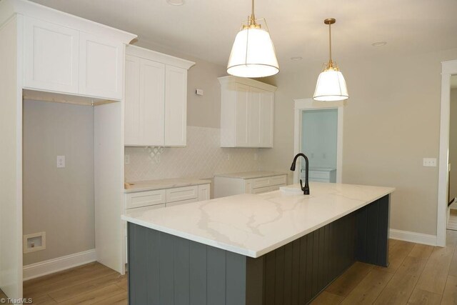 kitchen featuring light wood-type flooring, an island with sink, baseboards, white cabinets, and recessed lighting
