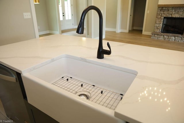 detailed view of a sink, light wood-type flooring, light stone countertops, and a stone fireplace