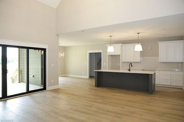kitchen featuring white cabinets, light wood finished floors, an island with sink, backsplash, and high vaulted ceiling