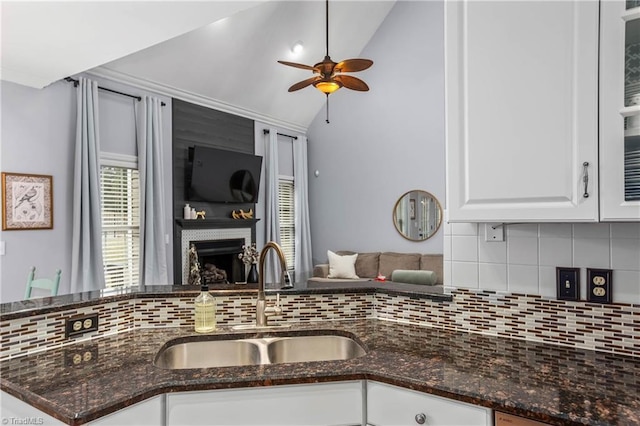 kitchen with sink, dark stone counters, white cabinetry, and lofted ceiling