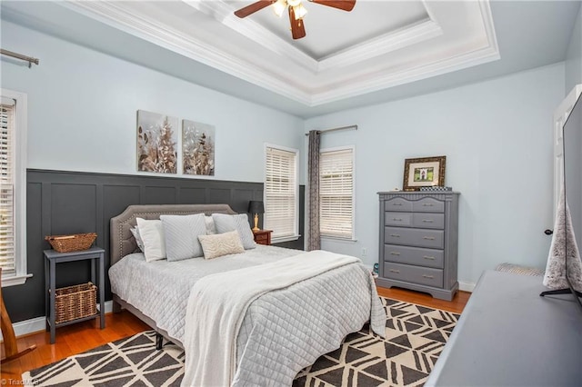 bedroom featuring ceiling fan, light wood-type flooring, a tray ceiling, and crown molding