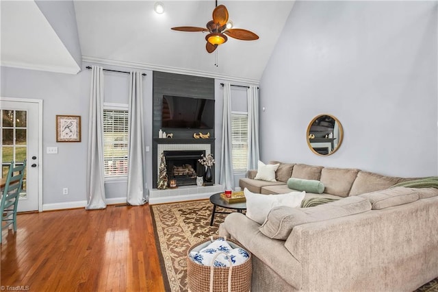 living room with ceiling fan, ornamental molding, vaulted ceiling, hardwood / wood-style flooring, and a tiled fireplace