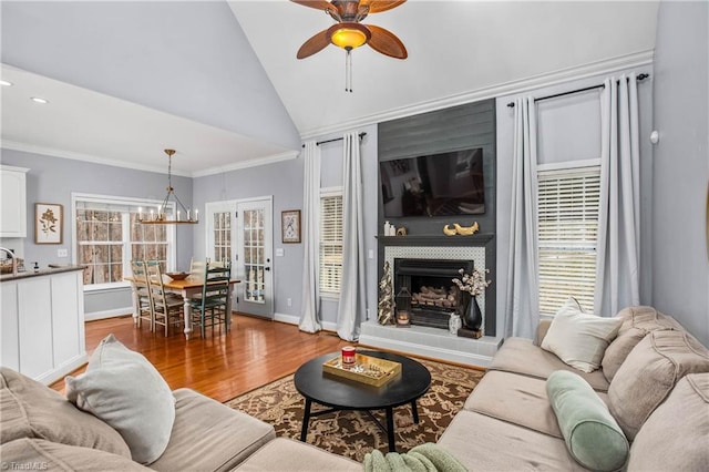 living room with ceiling fan with notable chandelier, a fireplace, light hardwood / wood-style floors, ornamental molding, and high vaulted ceiling