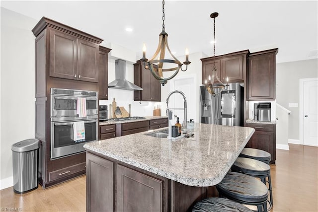 kitchen with stainless steel appliances, a kitchen island with sink, decorative light fixtures, wall chimney exhaust hood, and sink