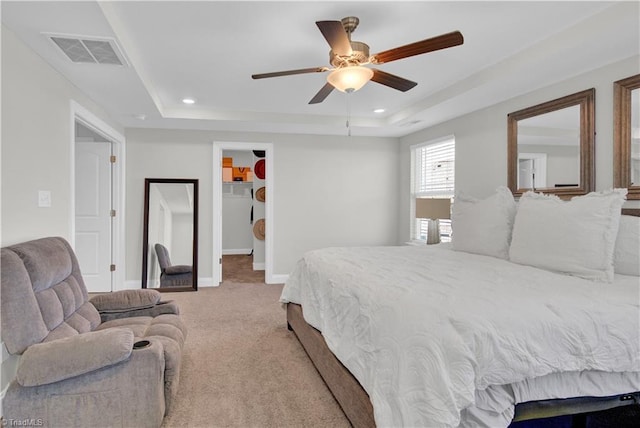 bedroom featuring ceiling fan, light colored carpet, a tray ceiling, a spacious closet, and a closet