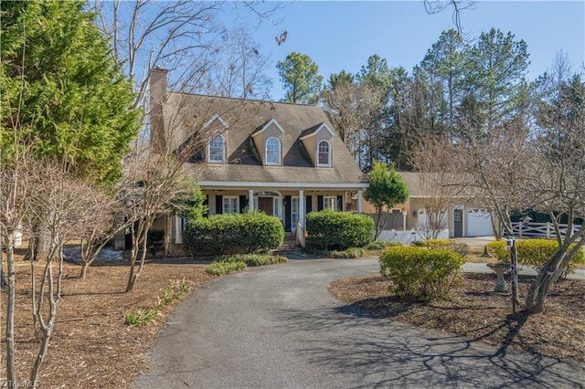 cape cod-style house with aphalt driveway, a chimney, and a garage