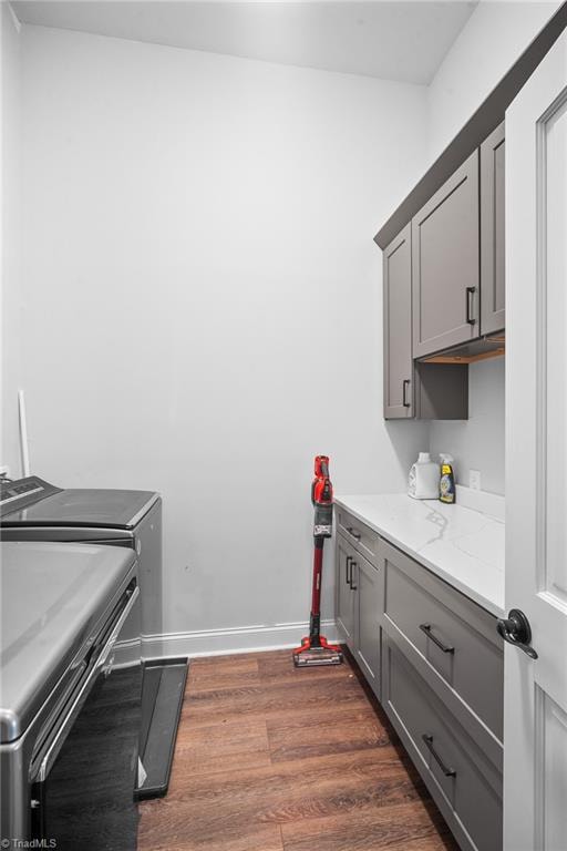 clothes washing area with washer and clothes dryer, cabinets, and dark hardwood / wood-style floors