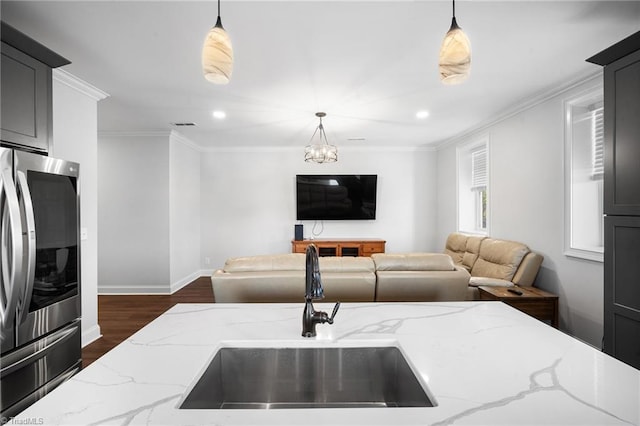 kitchen featuring light stone counters, hanging light fixtures, sink, and stainless steel refrigerator