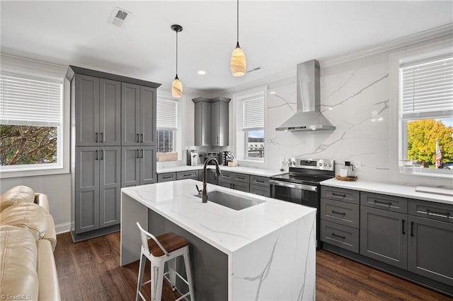 kitchen featuring gray cabinetry, a center island with sink, wall chimney range hood, decorative backsplash, and sink