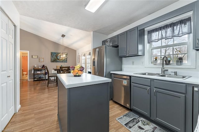 kitchen with stainless steel appliances, light countertops, vaulted ceiling, a sink, and a kitchen island