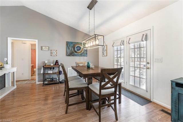 dining space with light wood finished floors, baseboards, visible vents, and high vaulted ceiling