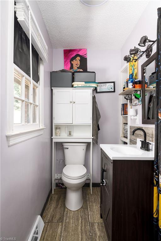 bathroom with a textured ceiling, wood finished floors, vanity, baseboards, and toilet
