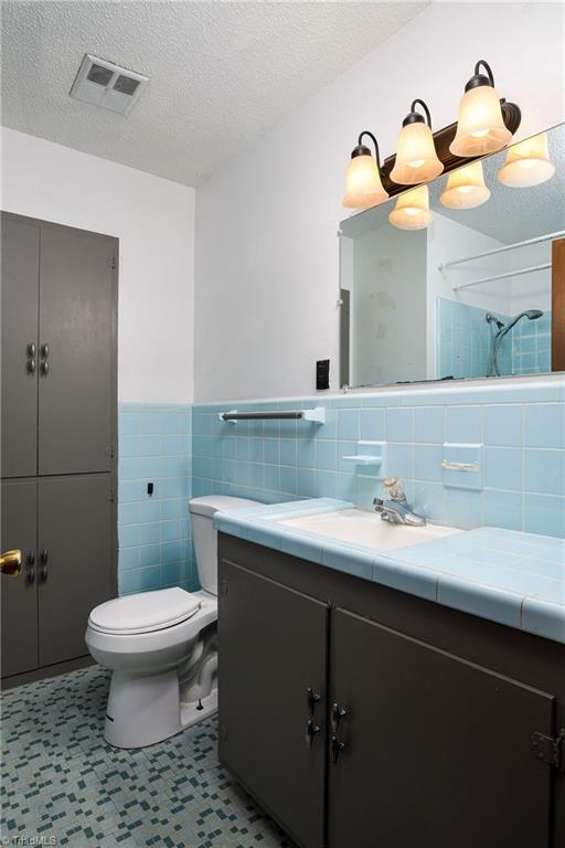 bathroom with wainscoting, vanity, toilet, tile walls, and visible vents